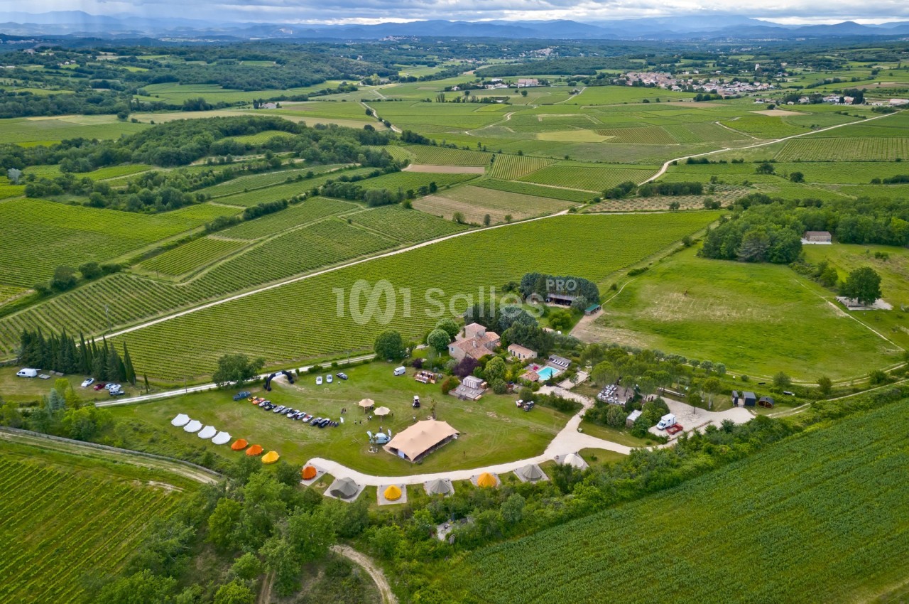 Vue aérienne d'un domaine rural avec des vignes, des bâtiments et des tentes entourés de champs verdoyants.