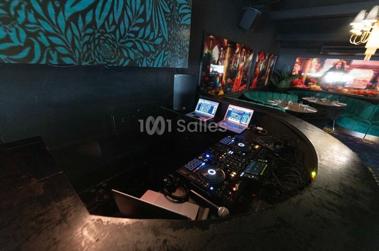 Poste de DJ avec platines, ordinateurs portables et câblage, dans un espace sombre décoré de motifs et de tableaux colorés.
