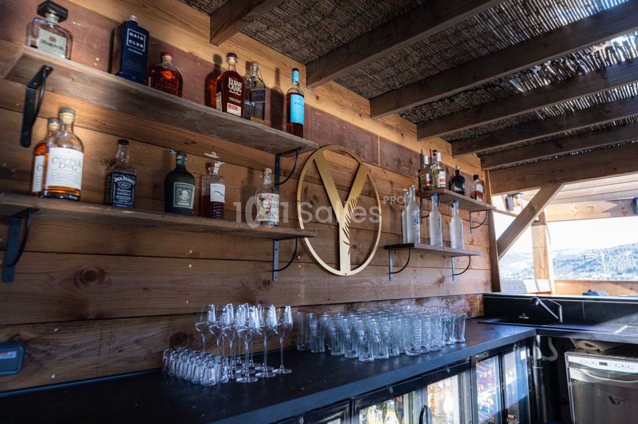 Étagères en bois garnies de bouteilles d'alcool et de verres, dans un bar extérieur à la structure en bois.