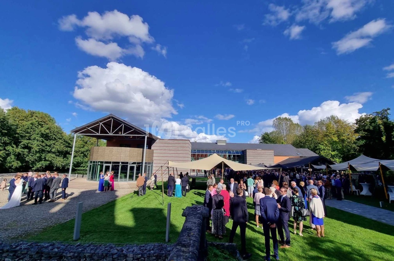 Groupe de personnes rassemblées en extérieur devant un bâtiment moderne sous un ciel bleu avec quelques nuages.