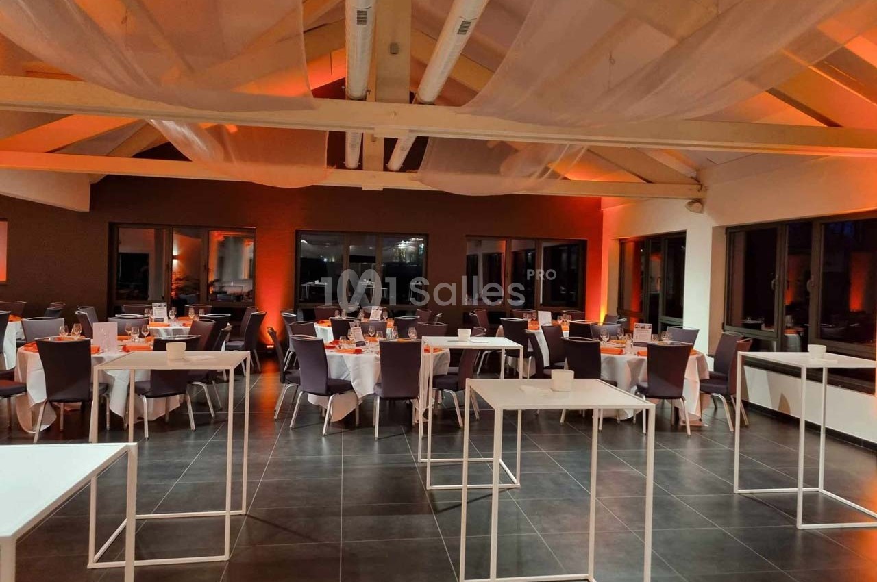 Salle de réception décorée avec des tables dressées, éclairage tamisé orange et plafond avec voilages suspendus.