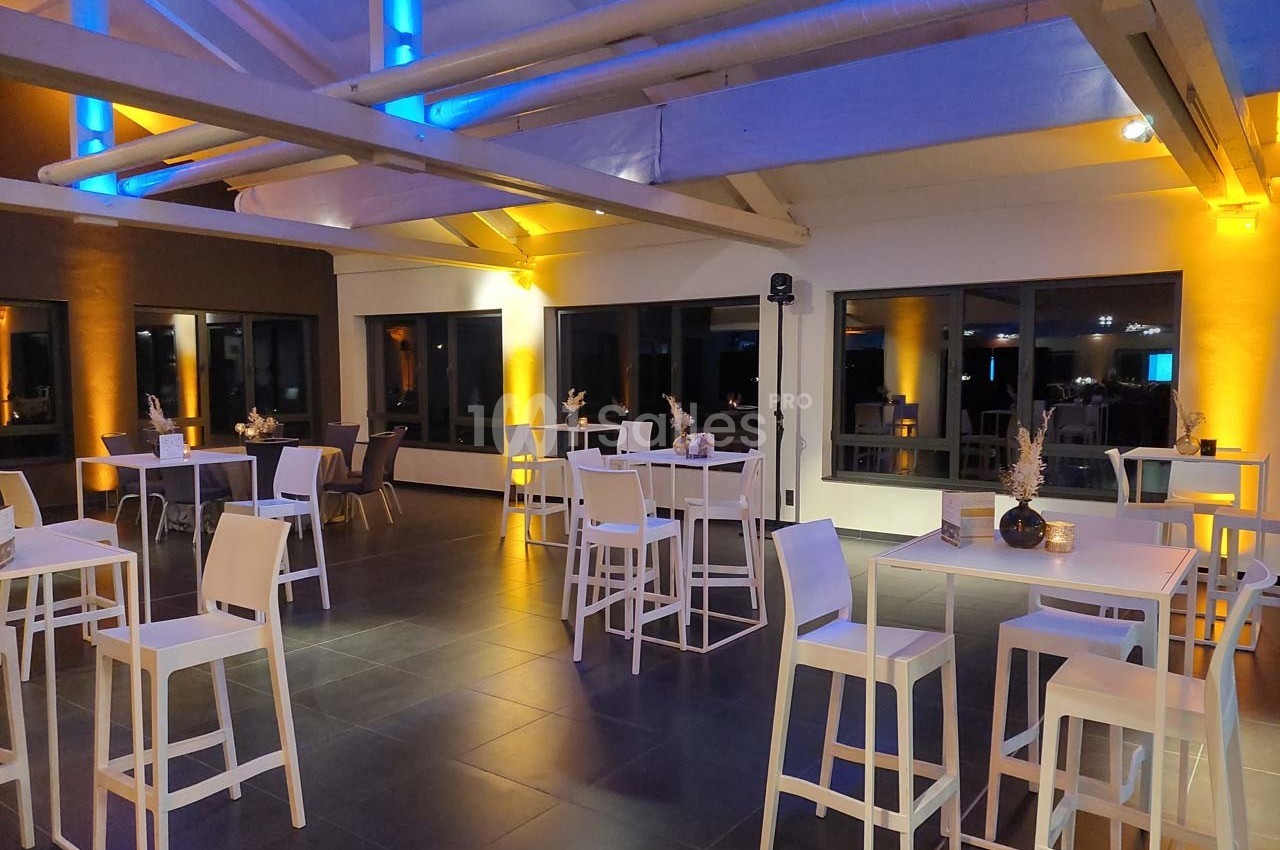 Salle moderne avec tables hautes blanches, chaises assorties et éclairage coloré bleu et jaune.