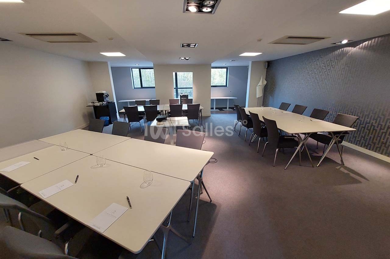 Salle de réunion lumineuse avec plusieurs tables disposées en U et en rangées, chaises et matériel de prise de notes.