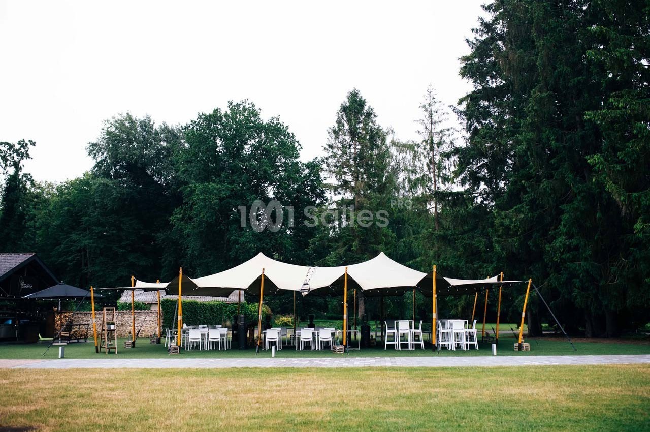 Tente blanche installée dans un jardin verdoyant, entourée de chaises et tables pour un événement en plein air.