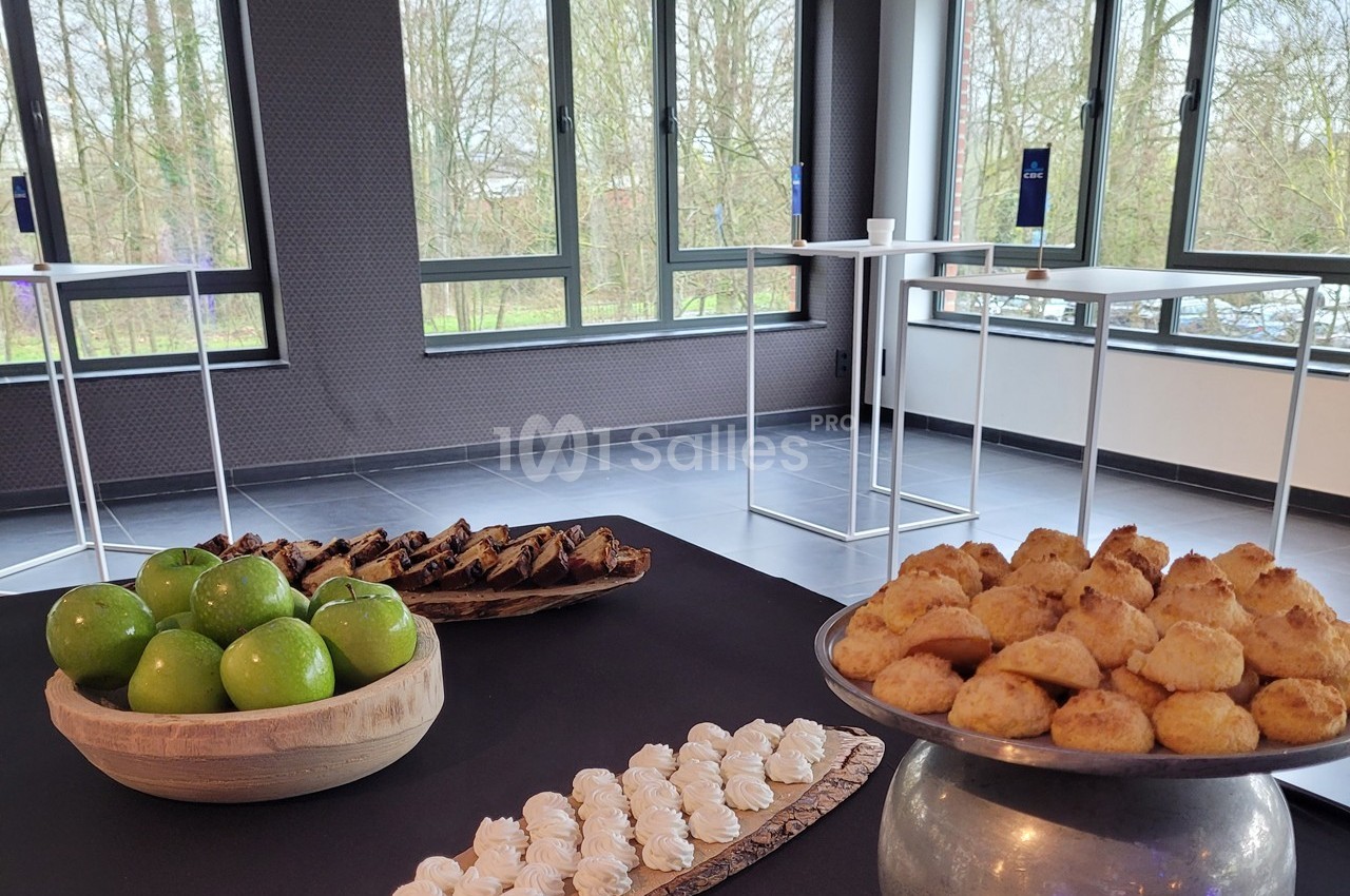 Table avec des desserts variés, des pommes vertes et des mignardises, dans une salle lumineuse avec vue sur des arbres.