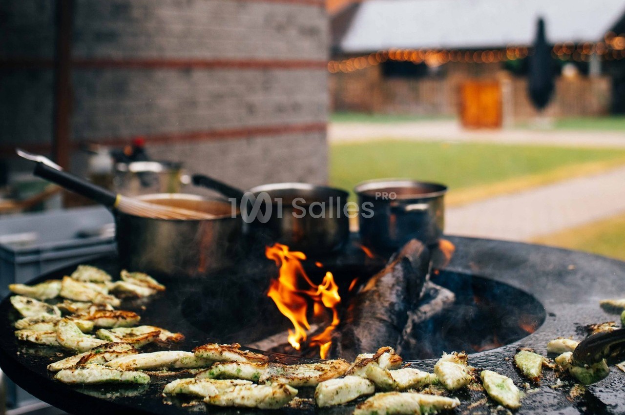 Légumes grillés sur une plaque chauffante au feu de bois, avec des casseroles en arrière-plan dans un espace extérieur.