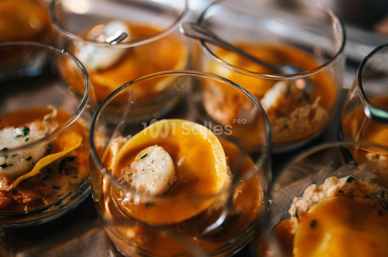 Ravioles servies dans des verrines avec une sauce orangée et une garniture de noix de Saint-Jacques.