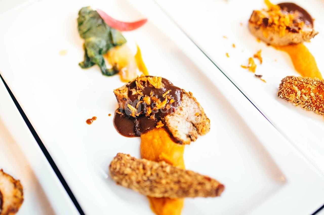 Assiette gastronomique avec viande, purée orange, légumes verts et croustillant, présentée sur une table blanche.