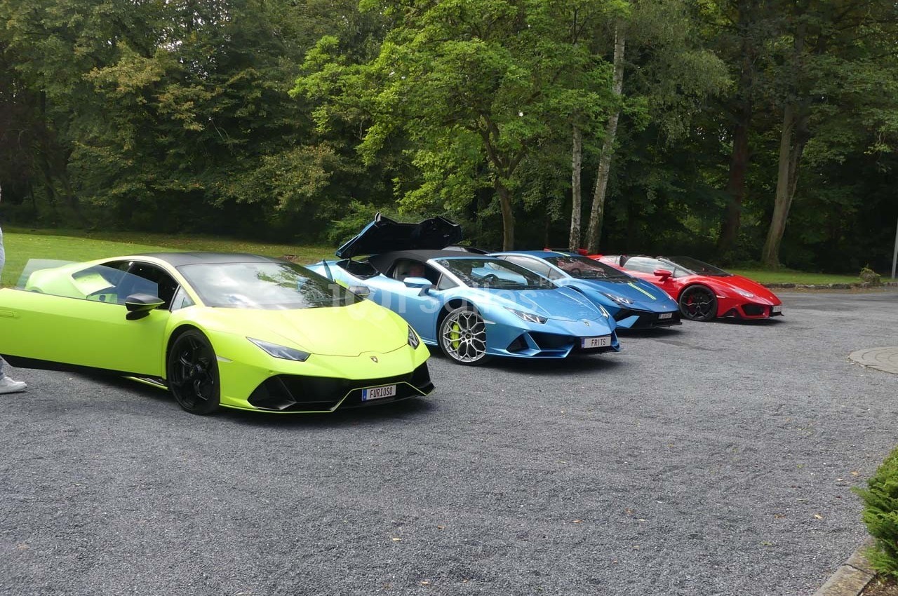 Quatre voitures sportives colorées alignées sur un parking en plein air, entourées de verdure.
