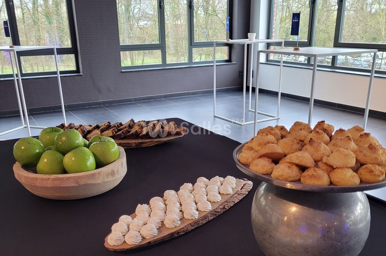 Plateau de desserts variés avec pommes vertes, meringues, biscuits et gâteaux dans une salle lumineuse.