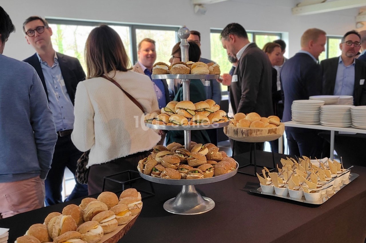 Plateau de mini-sandwichs et verrines sur une table lors d'un événement avec des participants en arrière-plan.