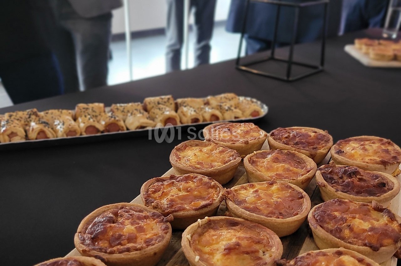 Plateau de mini-quiches au premier plan et assortiment de feuilletés en arrière-plan sur une table noire.