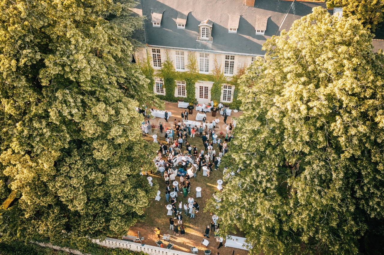 Vue aérienne d'un rassemblement en plein air dans la cour d'un bâtiment historique entouré d'arbres.