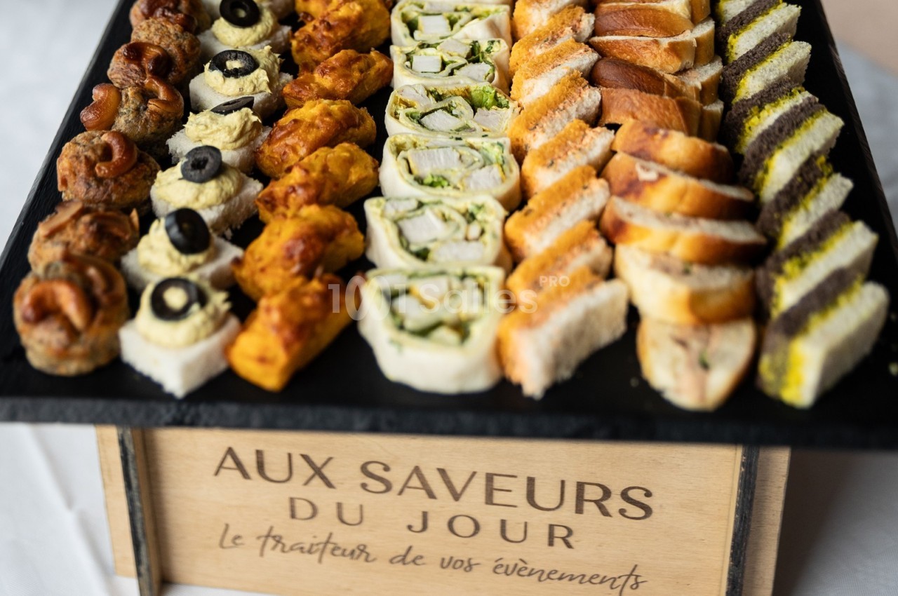 Plateau de canapés variés comprenant des bouchées salées, roulés et mini-sandwichs présentés sur un support en bois.