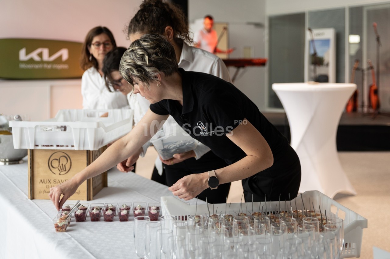 Une femme dispose des verrines sur une table lors d'un événement, avec d'autres personnes en arrière-plan.