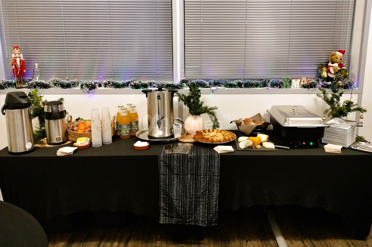 Table de buffet avec boissons chaudes, jus, viennoiseries, fruits et décorations festives.