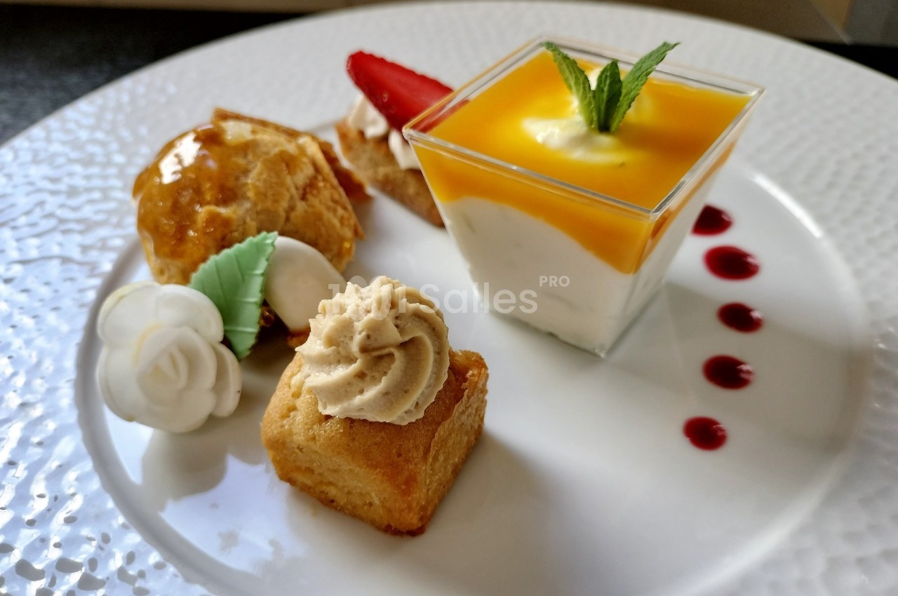 Assortiment de desserts comprenant une verrine au coulis de mangue, des gâteaux décorés et une fraise tranchée.
