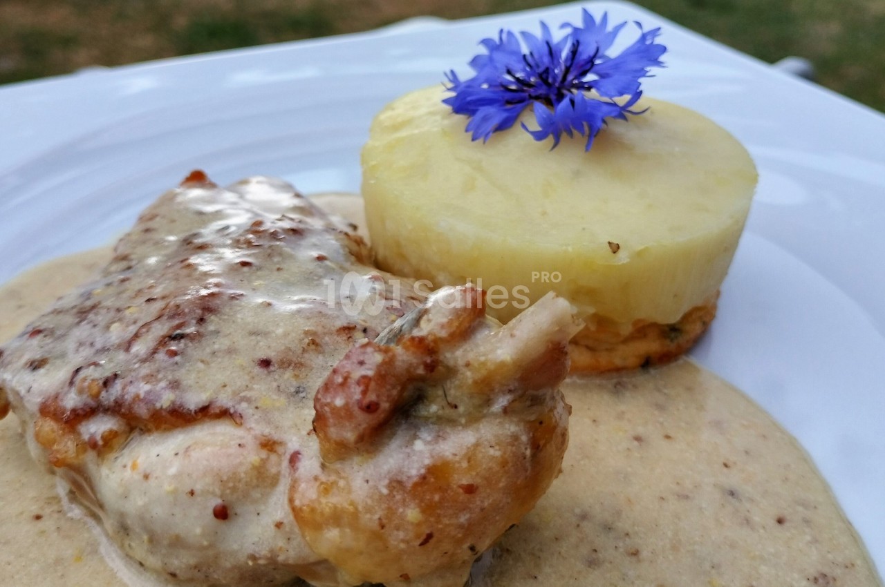 Plat de poulet à la sauce moutarde, accompagné d'un gratin de pommes de terre décoré d'une fleur bleue.