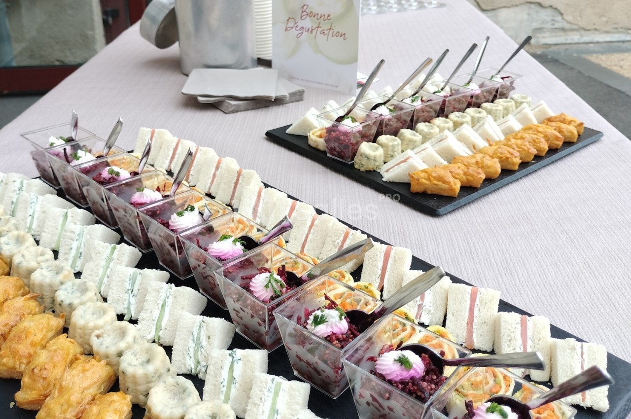 Plateau de verrines, mini-sandwichs et bouchées salées disposés sur une table pour un buffet.