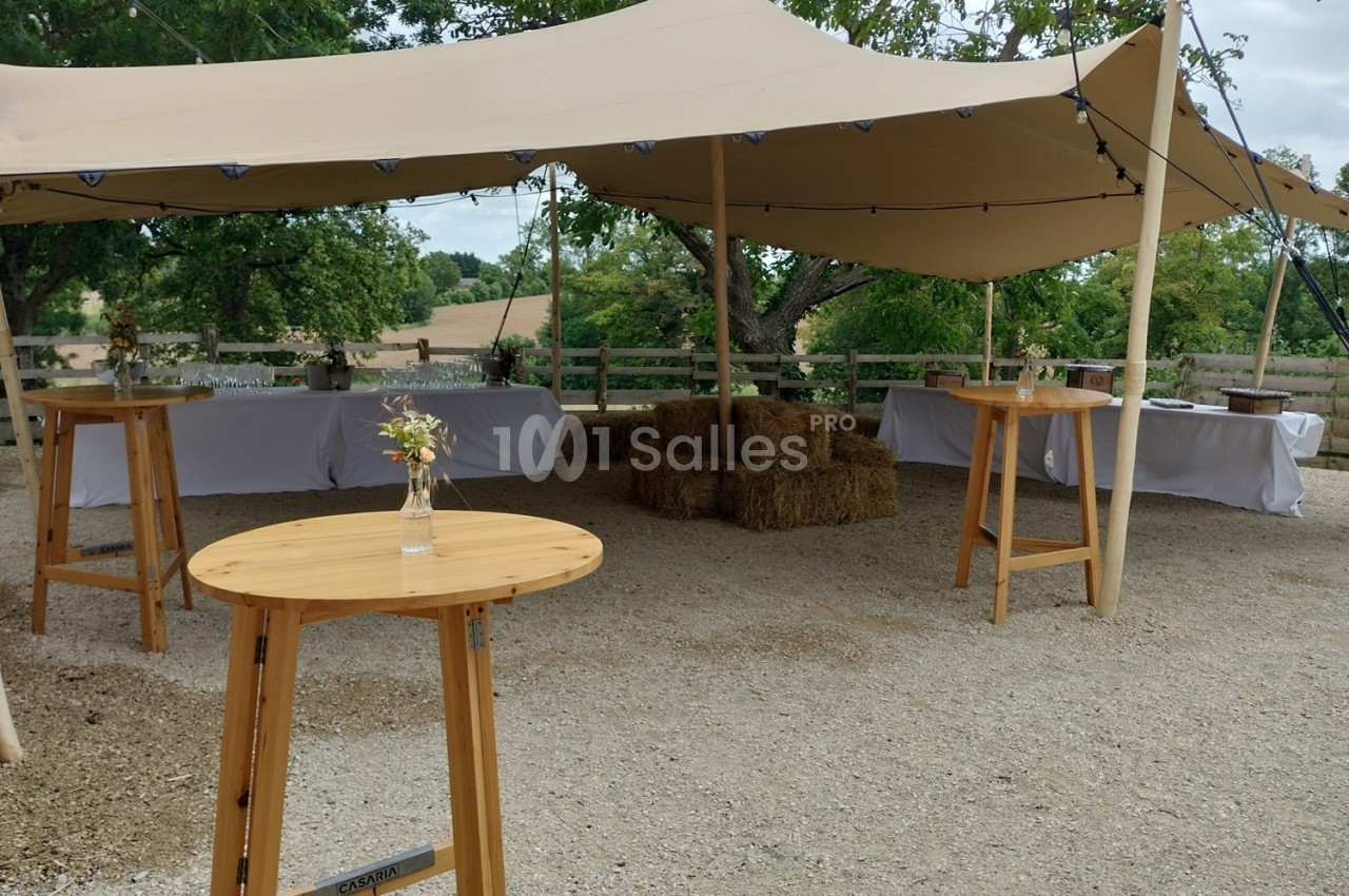Tente beige avec tables en bois, bottes de paille et tables dressées en arrière-plan dans un cadre champêtre.