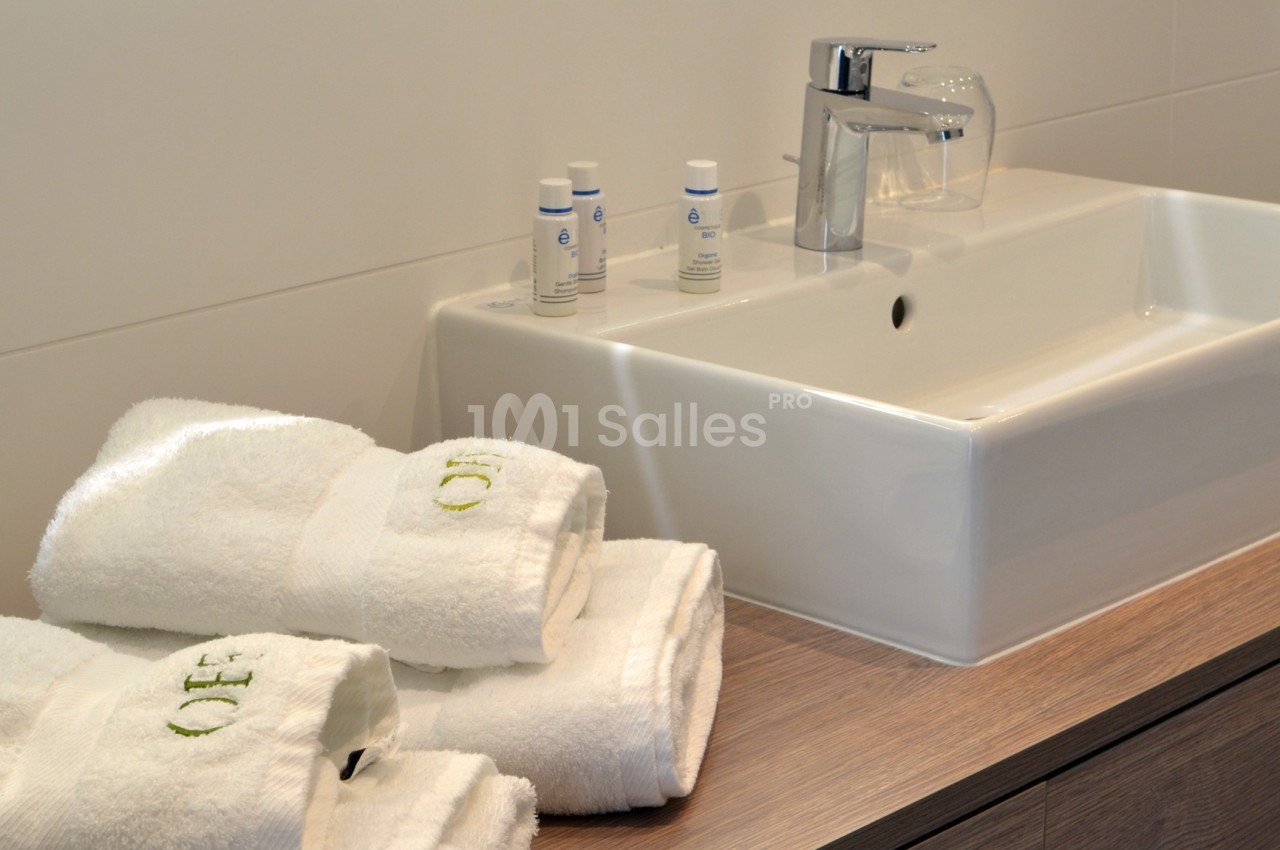 Lavabo moderne avec robinet chromé, serviettes blanches pliées et produits de toilette disposés sur un plan en bois.