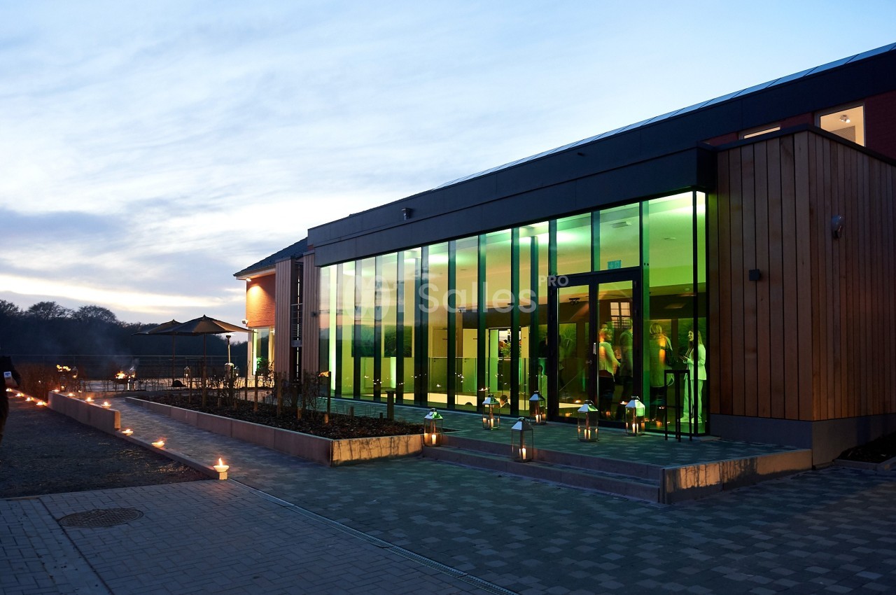 Bâtiment moderne avec façade vitrée illuminée, entouré de bougies au crépuscule.