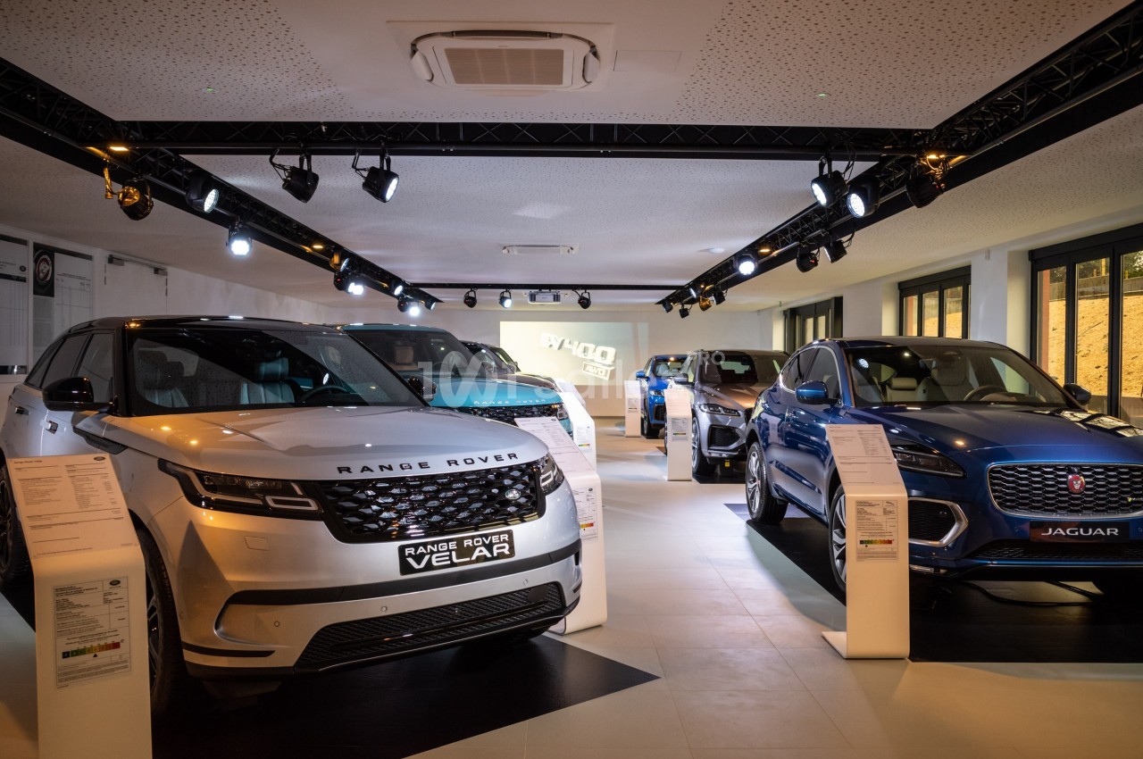 Exposition de véhicules Range Rover et Jaguar dans un showroom éclairé avec des fiches techniques visibles.