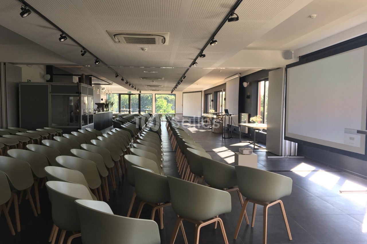 Salle de conférence lumineuse avec des rangées de chaises modernes et des écrans de projection en arrière-plan.