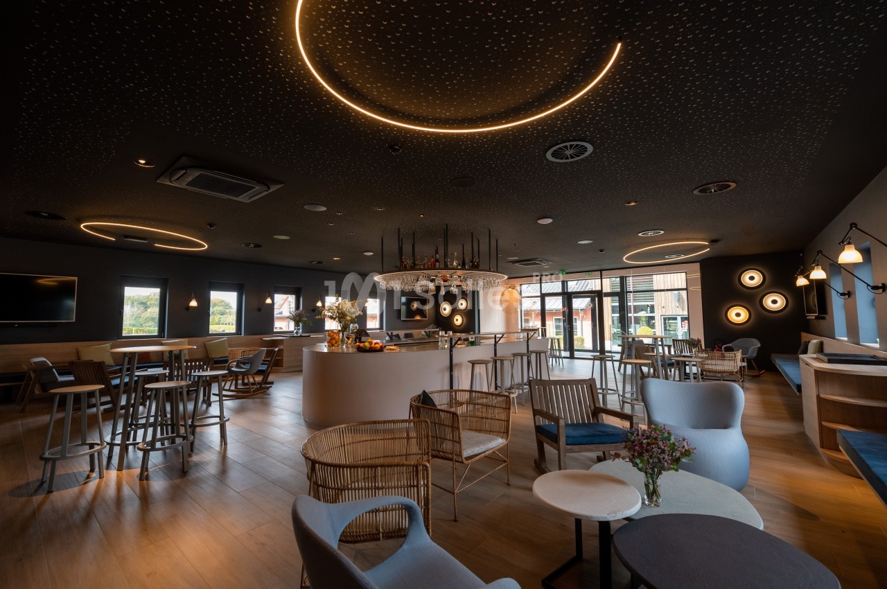 Salle moderne avec éclairage tamisé, mobilier varié et grandes fenêtres donnant sur l'extérieur.