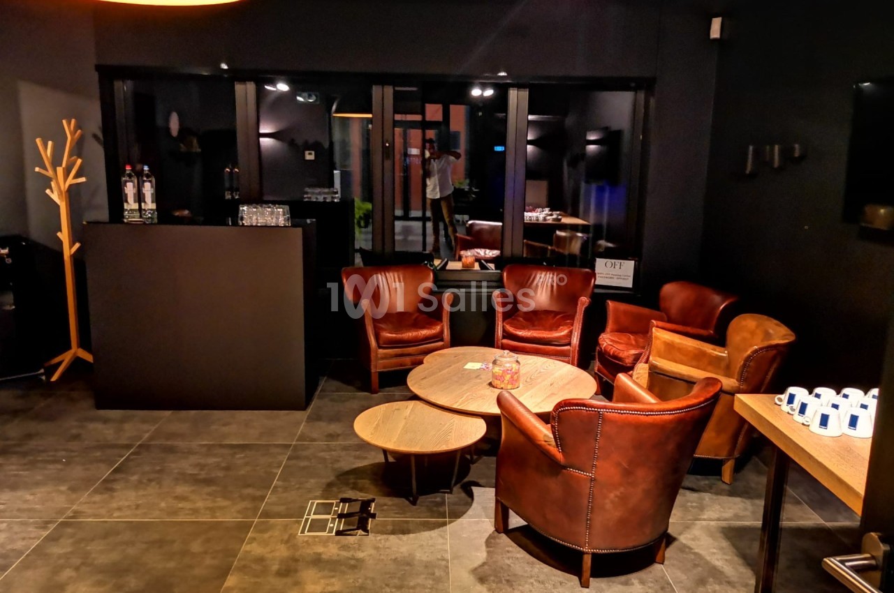 Espace lounge avec fauteuils en cuir, tables basses en bois et éclairage tamisé dans une ambiance moderne.