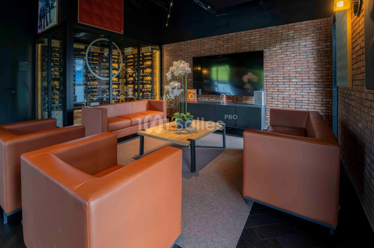 Salle de séjour moderne avec canapés en cuir orange, table basse en bois, écran mural et mur en briques apparentes.