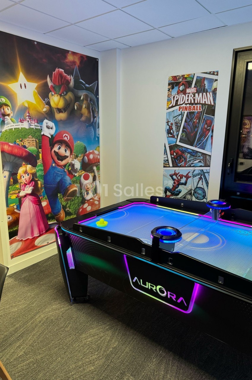 Table de air hockey lumineuse dans une salle décorée avec des affiches de Mario et Spider-Man.