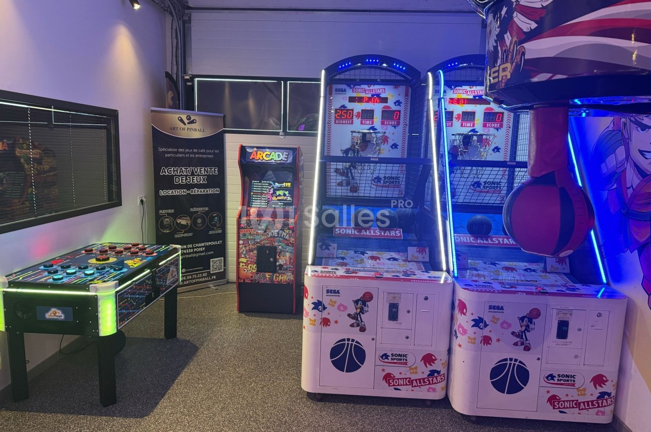 Salle de jeux avec baby-foot, bornes d'arcade et machines de basket lumineuses dans un espace intérieur.