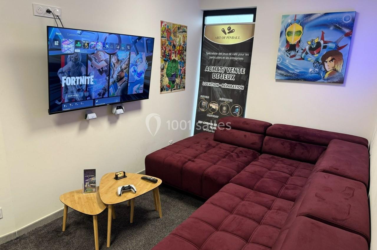 Salle de jeux avec canapé d'angle, écran affichant un menu de jeu vidéo, table basse et affiches décoratives au mur.