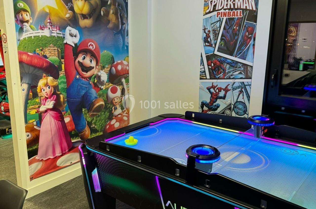 Table de air hockey éclairée avec des affiches de Mario et Spider-Man en arrière-plan dans une salle de jeux.