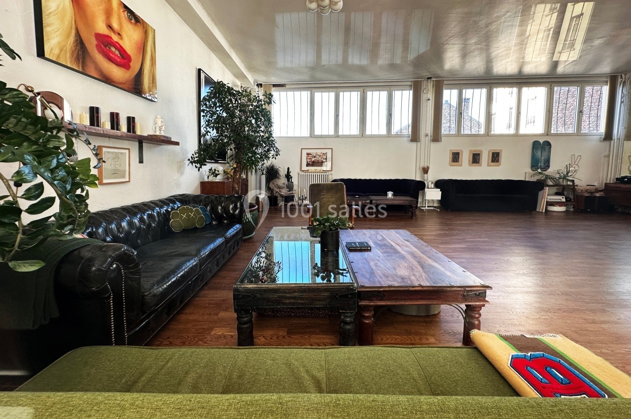 Salon spacieux avec canapés en cuir, table basse en bois, plantes et grandes fenêtres laissant entrer la lumière naturelle.