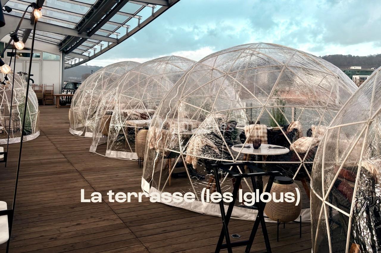 Terrasse en bois avec des igloos transparents aménagés pour des repas en extérieur, vue sur un paysage naturel.