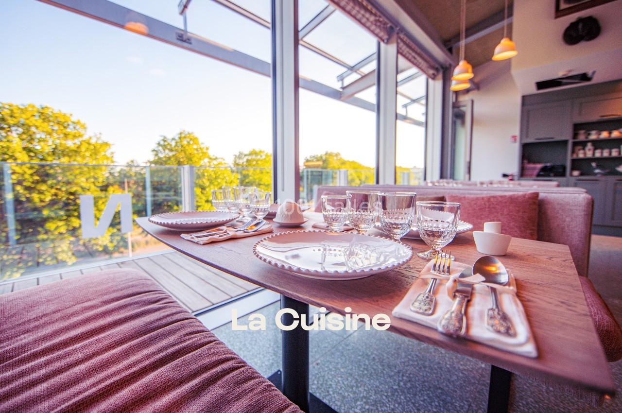 Table dressée avec vaisselle élégante, vue sur une terrasse ensoleillée et des arbres à travers de grandes baies vitrées.