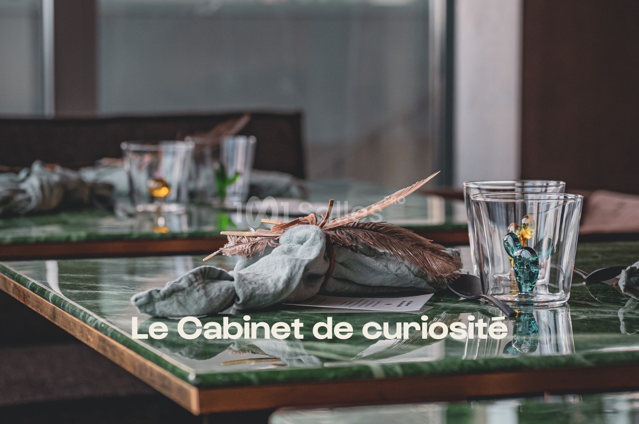 Table en marbre vert avec serviette pliée, plume décorative et verres, dans un cadre intérieur lumineux.