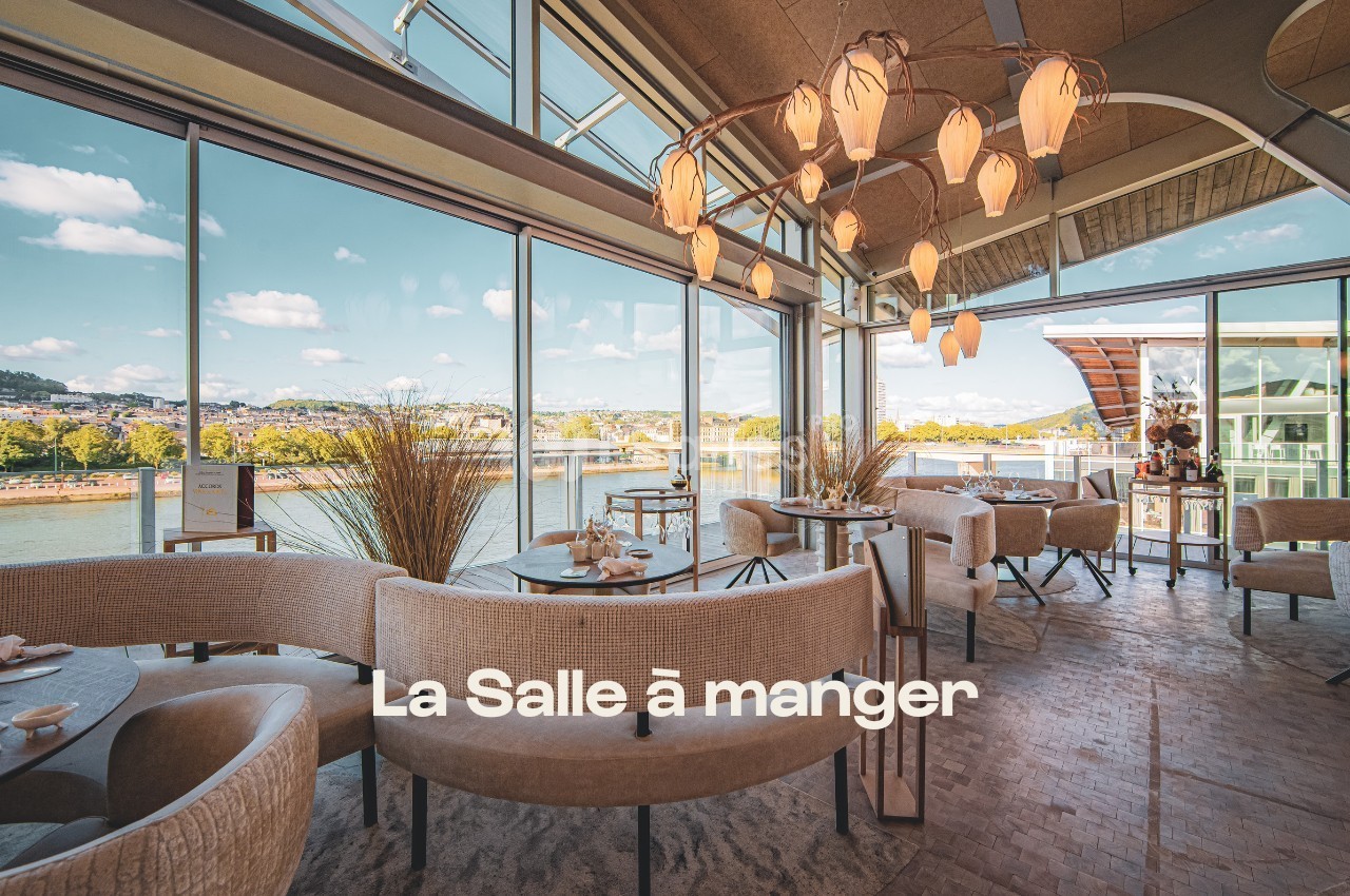 Salle de restaurant lumineuse avec grandes baies vitrées donnant sur un paysage fluvial et un lustre design.