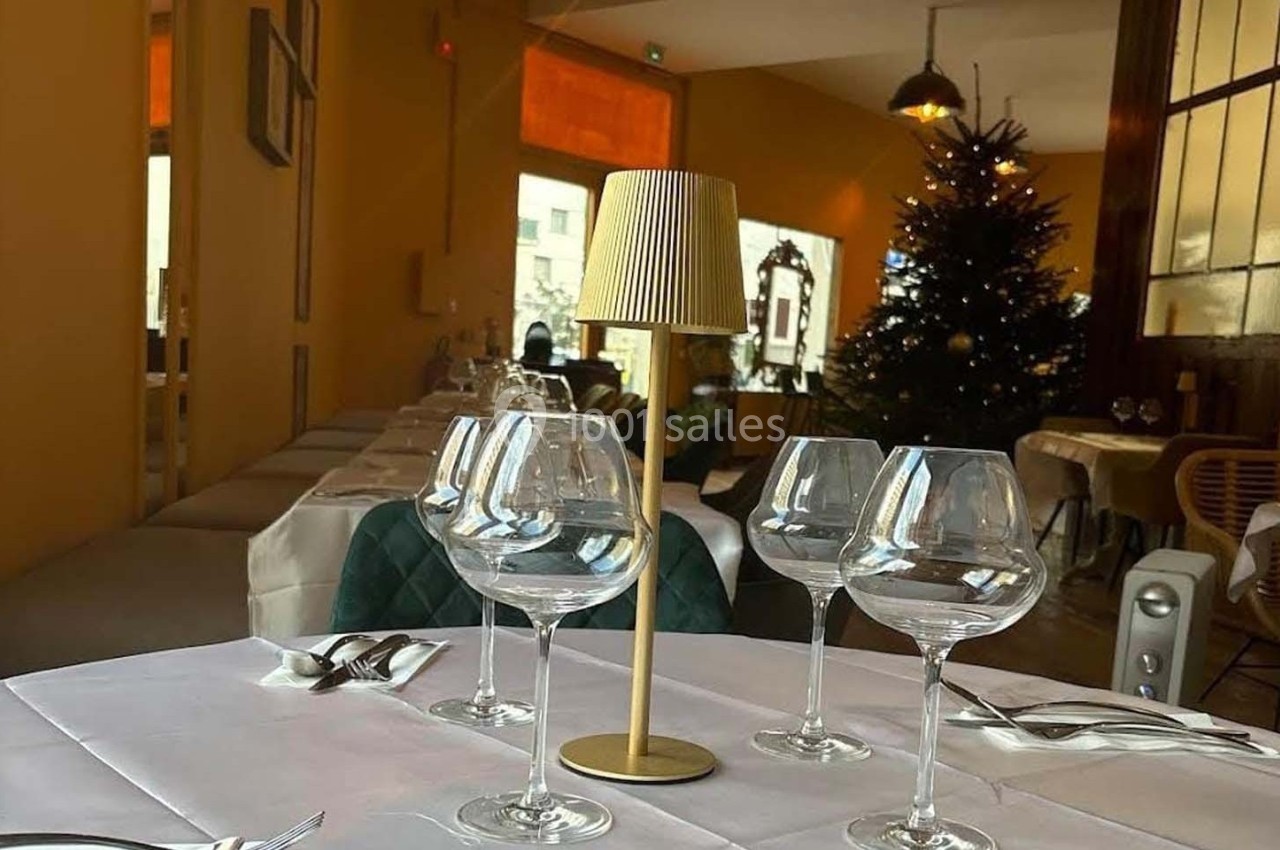 Table dressée avec des verres à vin et une lampe, dans un restaurant décoré avec un sapin de Noël en arrière-plan.