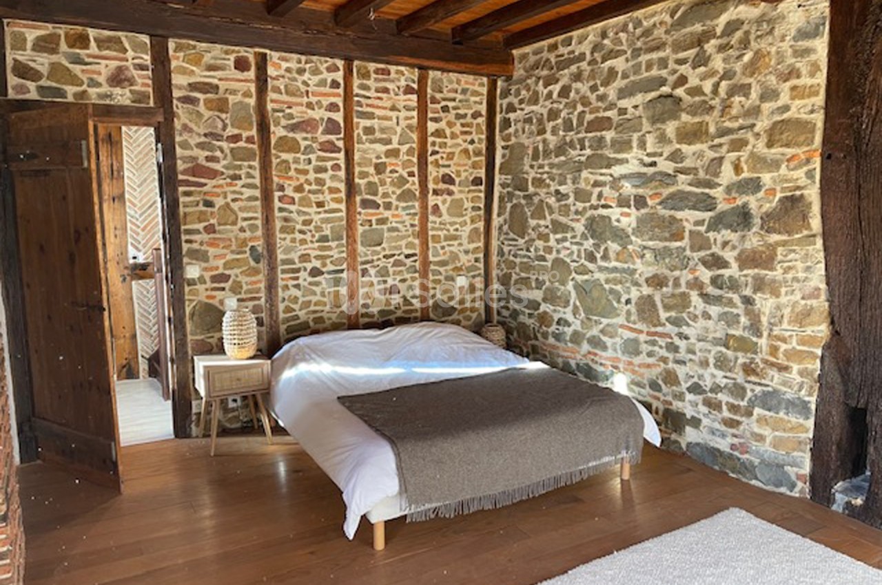 Chambre avec murs en pierre apparente, poutres en bois, lit double, parquet et lumière naturelle.