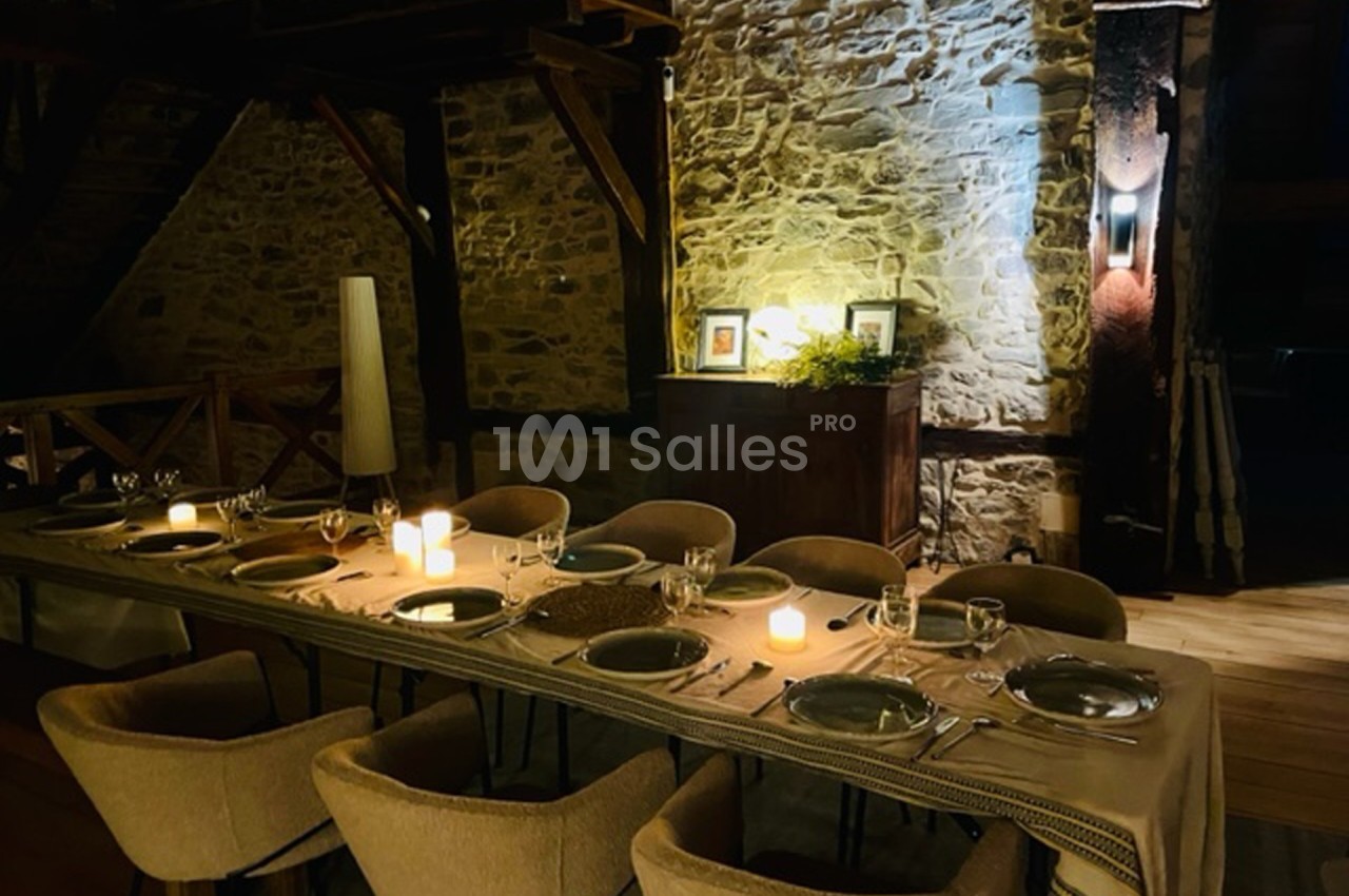 Table élégamment dressée avec bougies allumées dans une salle en pierre apparente, ambiance chaleureuse et intime.