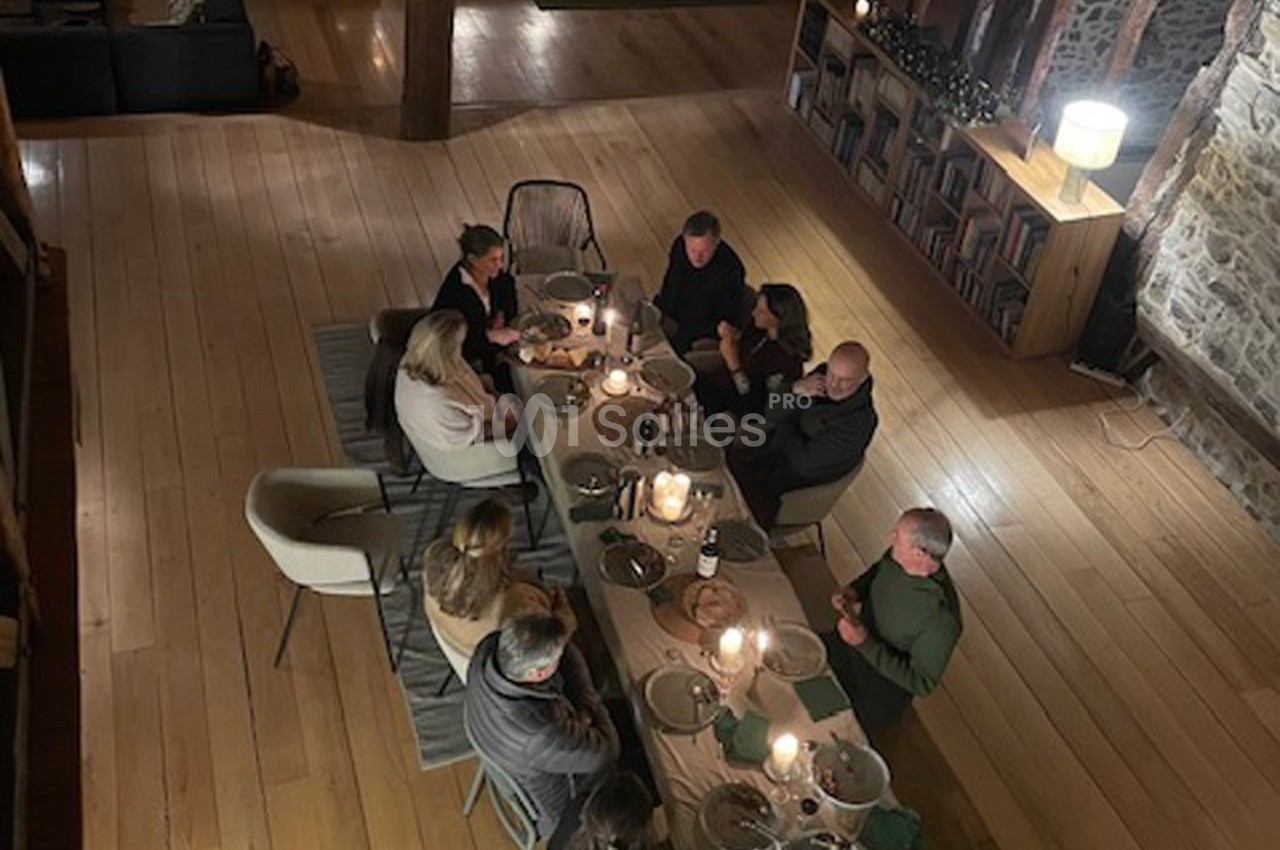 Vue plongeante d'un groupe de personnes partageant un repas autour d'une table éclairée par des bougies dans une pièce…