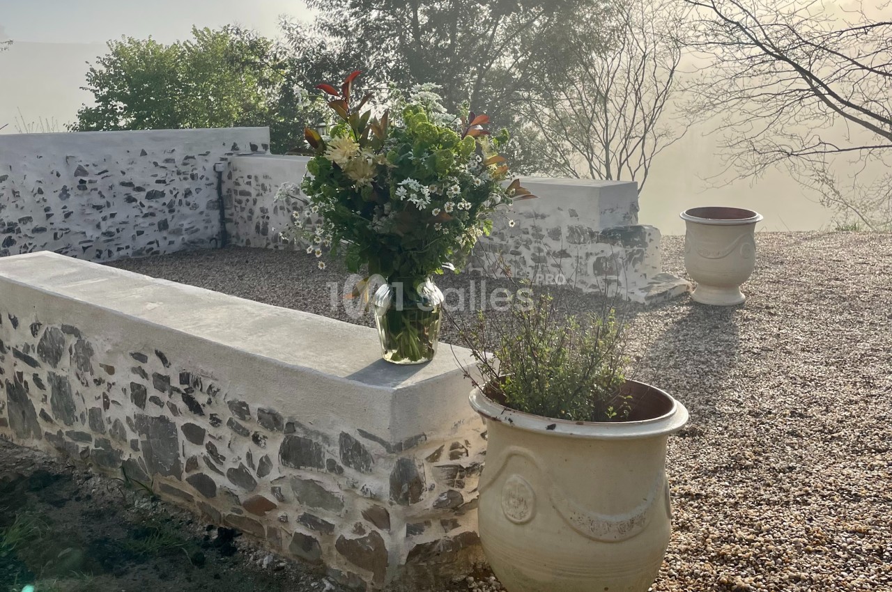 Un bouquet de fleurs posé sur un muret en pierre, entouré de pots et d'un paysage brumeux.