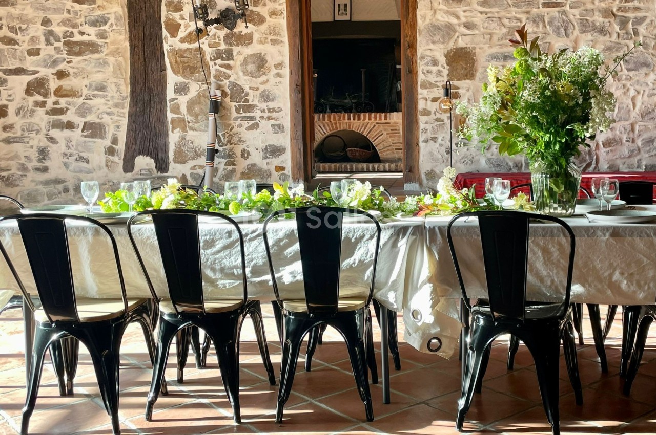 Table dressée avec une nappe blanche, chaises noires et décoration florale, dans une pièce aux murs en pierre.