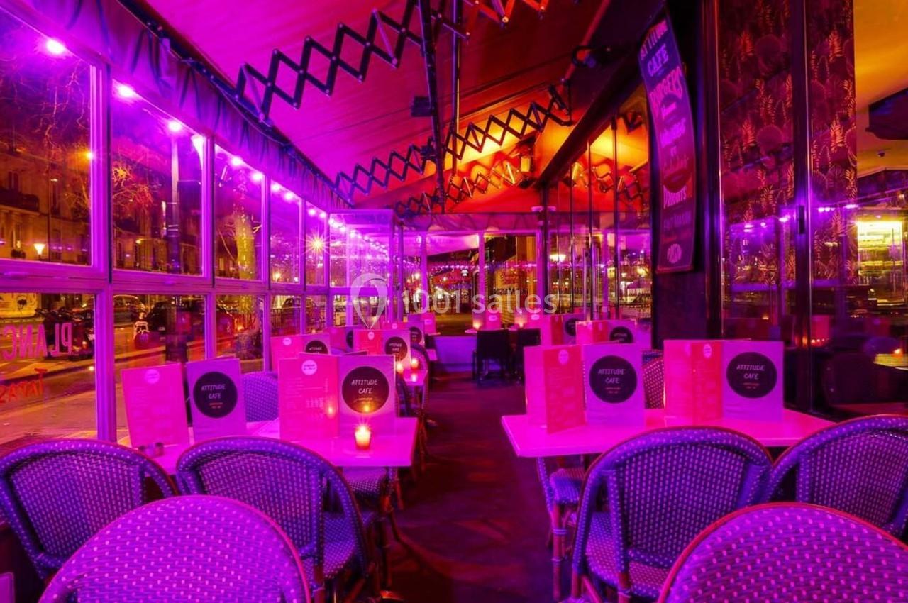 Terrasse de restaurant éclairée par des lumières violettes, avec des tables et chaises en osier disposées en rangées.