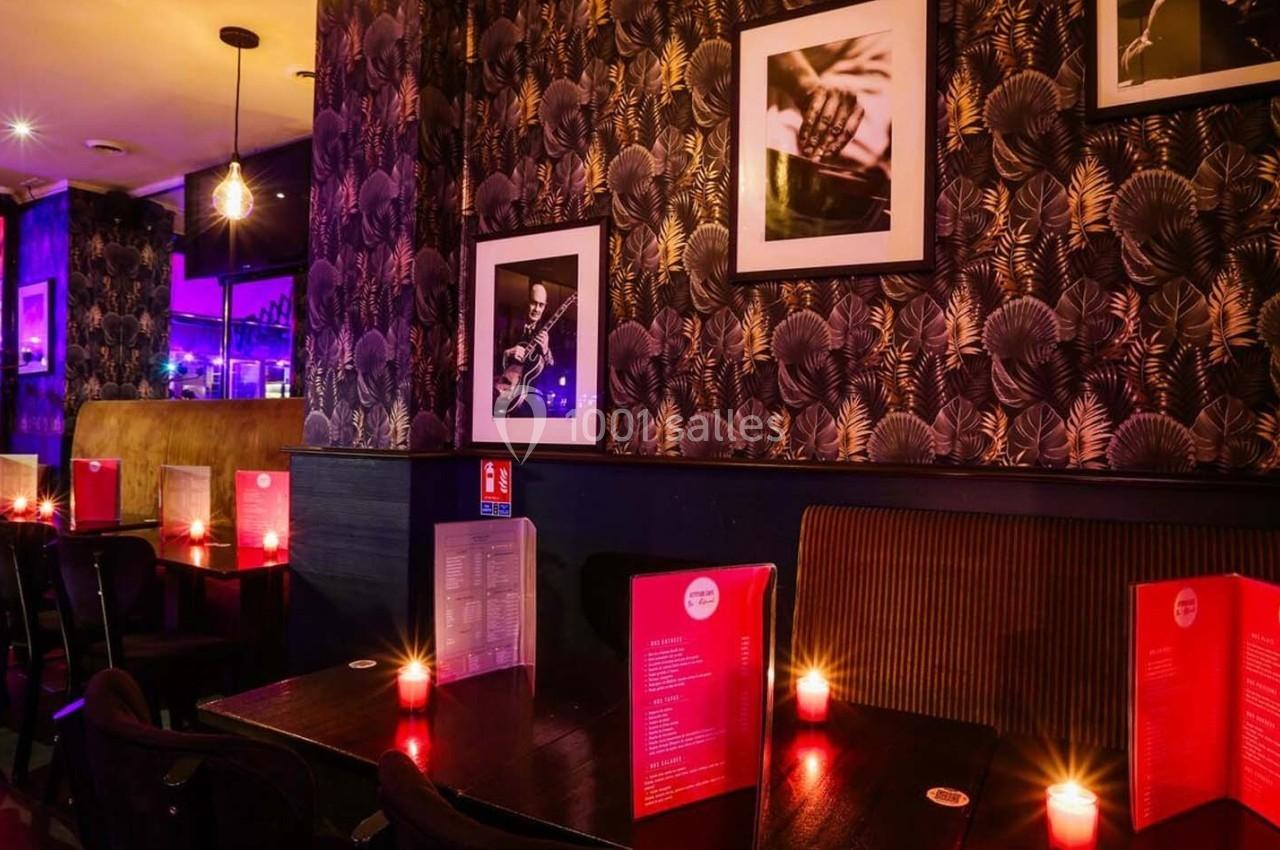 Salle de restaurant avec tables éclairées par des bougies, décorée de papiers peints sombres et photos encadrées.