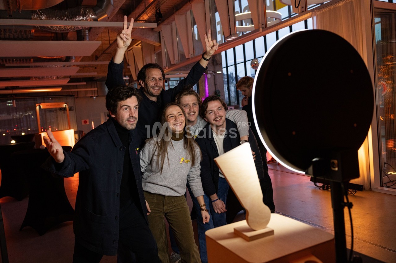 Un groupe de personnes souriantes pose devant un photobooth dans un espace intérieur moderne et lumineux.