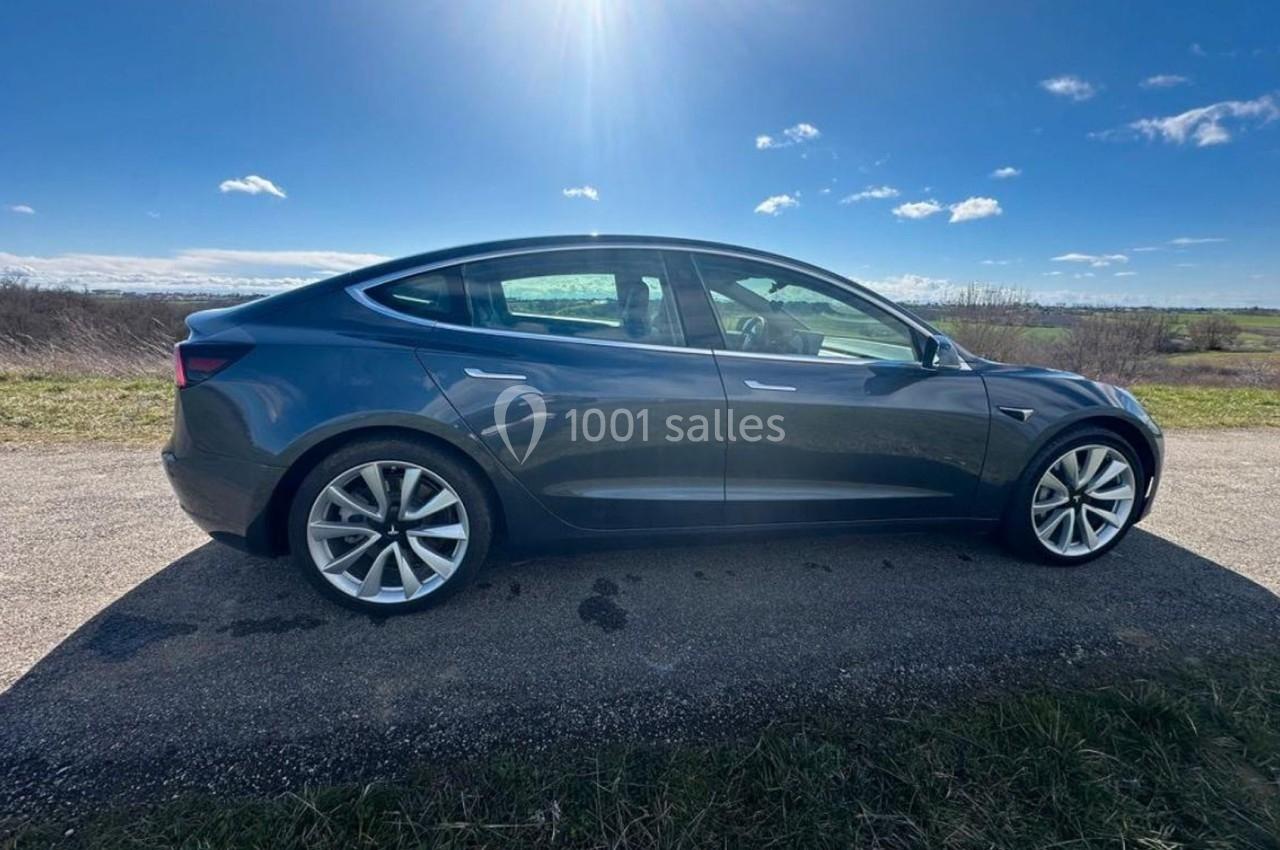 Voiture électrique grise stationnée sur une route de campagne sous un ciel ensoleillé.